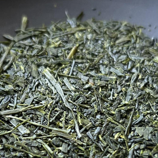 A close-up of loose-leaf green tea leaves piled in a dark gray bowl.